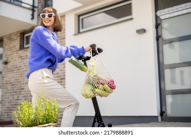 Happy stylish woman going home with fresh vegetables in mesh bag, driving on electrical scooter at residential district. Concept of modern eco-friendly lifestyle and sustainability - Powered by Shutterstock