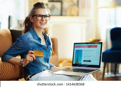 Happy Stylish Woman With Opened On Laptop Online Travel & Booking Agency Site Holding Credit Card In The Modern House In Sunny Summer Day. A Fake Website Is Made For Illustrative Purposes.