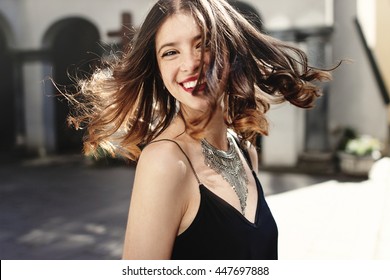 happy stylish woman waving hair in sunlight at old european city street, luxury look, space for text, moment of carefree and true happiness