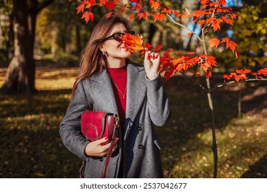 Happy stylish woman wears trendy autumn outfit. Woman wearing grey fall coat, holding burgundy leather purse outdoors. Fall fashion - Powered by Shutterstock