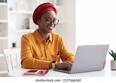 Happy Stylish Young Black Lady In Red Turban Freelancer Working On Laptop, Typing On Computer Keyboard, Sending Emails Or Chatting With Clients, Home Interior, Copy Space. Remote Job Concept