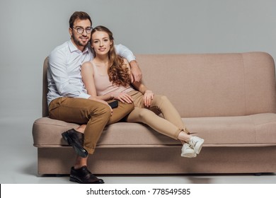 Happy Stylish Young Couple With Smartphone Smiling At Camera While Sitting Together On Sofa Isolated On Grey