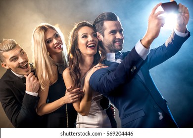 Happy stylish young friends taking selfie with smartphone while celebrating