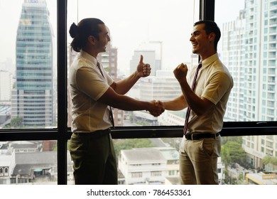 The Happy And Success Business Man With Window View Of The High Building Office.Two Men Shaking Hands Standing At Big Window With Urban Cityscape, Confident Business Partner. Forming Good Relationship