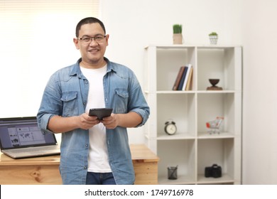 Happy successful Asian male holds tablet checking his online business, modern casual entrepreneur with electronic device wireless gadget, looking at camera and smile, browse websites, freelancer worki