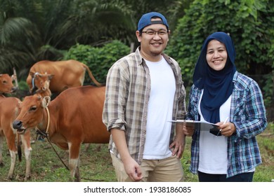 Happy Successful Asian Muslim Farmer Couple Looking At Camera And Smiling, With Domesticated Cow Ox Cattle Grazing In The Background, Organic Agriculture Farming Entrepreneur