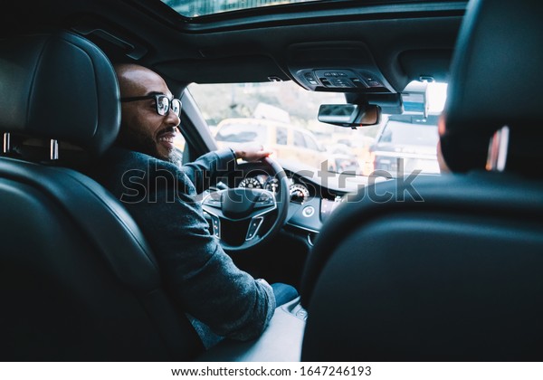 Happy successful bald and bearded male manager in\
glasses and formal clothes having conversation with colleague and\
driving corporate car