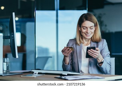 Happy and successful business woman shopping online, working in a modern office, an employee uses a phone for shopping and an application, holding a credit card