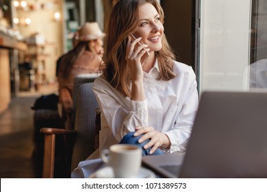 Happy erfolgreiche Geschäftsfrau telefoniert mit dem Handy in der Kaffeebar, lächelnde Unternehmerin mit Laptop und mit dem Handy in Cafe zu sprechen, Konzept der Fernarbeit