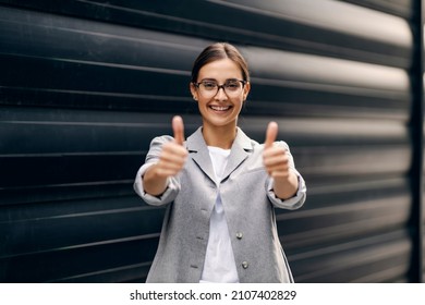A happy successful businesswoman standing outdoors and showing thumbs up with both hands. The business is going very well