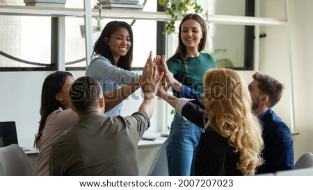 Happy successful diverse team giving high five, sitting in circle on meeting, discussing business project success, work result, teamwork achieve. Group making unity gesture, expressing high motivation