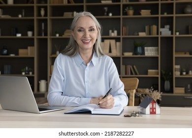 Happy Successful Elderly Realtor Woman, Real Estate Agent, Mortgage Broker Sitting At Table With Notebook, Laptop, Tiny Model Of Family House And Keys, Looking At Cameral Smiling. Head Shot Portrait