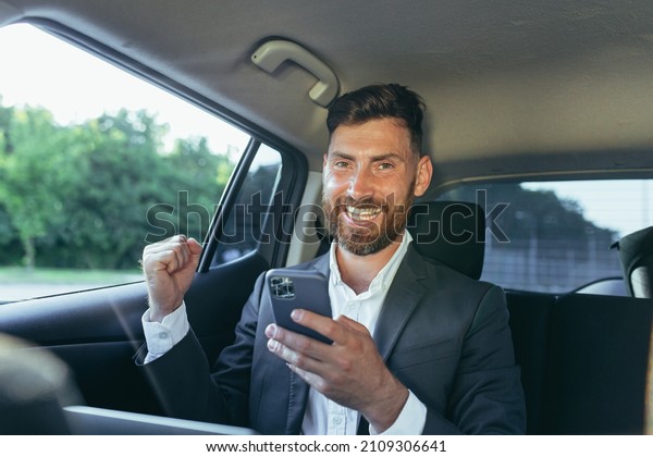 Happy and successful male businessman car\
passenger reads the news from the phone, rejoices in the victory\
and the news received