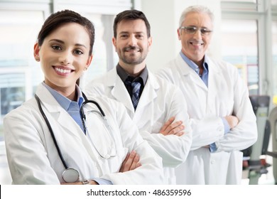 Happy successful medical team in a hospital standing in their white lab coats with folded arms in a receding staggered row with focus to an attractive female doctor in front in a healthcare concept