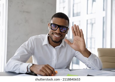 Happy successful millennial African business leader in glasses waving hand hello, looking at camera with toothy smile, making video call from office, negotiating on online conference chat