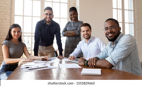 Happy successful multiracial business team gathered in modern boardroom for brainstorming working together on project posing look at camera teamwork representative of smart skilled specialists concept