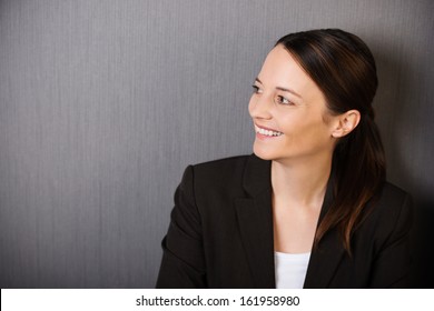 Happy Successful Professional Woman With A Lovely Broad Smile Looking Sideways, Head And Shoulders Portrait On Grey With Copyspace