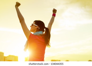 Happy successful sportswoman raising arms to the sky on golden back lighting sunset summer. Fitness athlete with arms up celebrating goals after sport exercising and working out outdoors. Copy space. - Powered by Shutterstock