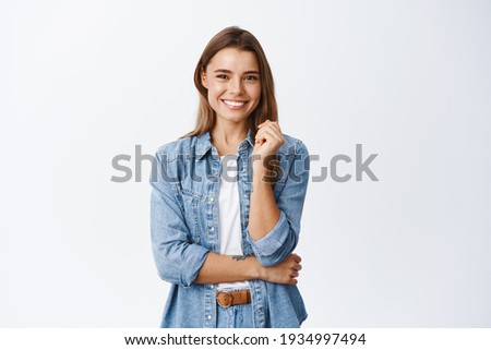 Photo of Happy successful woman standing in casual outfit, smiling pleased at camera and looking confident, standing against white background