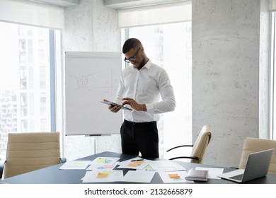 Happy successful young African American businessman in formal wear using digital computer tablet applications, standing near table with paper documents, working distantly or consulting client online. - Powered by Shutterstock