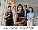 Happy successful young Middle Eastern project leader woman posing with for portrait, standing on front of diverse business team, looking at camera, enjoying leadership, group support