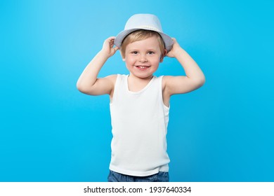 Happy Summer Boy In White T-shirt And Hat On A Blue Background With Copy Space. Tank Top Mockup. Summer Kid, Travel Concept.