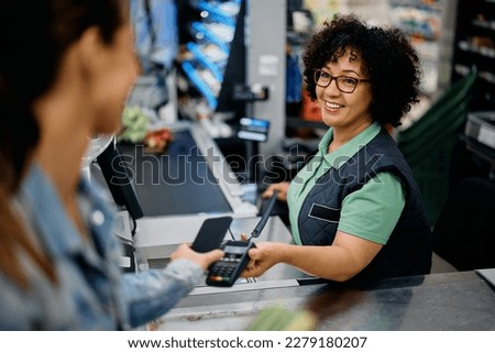 Happy supermarket cashier accepting mobile payment from a customer at store checkout.