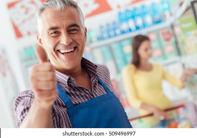 Happy supermarket clerk smiling and giving a thumbs up, he is smiling at camera
