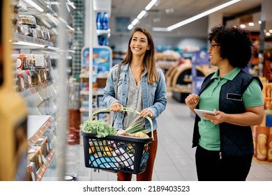 Happy supermarket manager assisting young woman in buying food at refrigerated section.  - Powered by Shutterstock