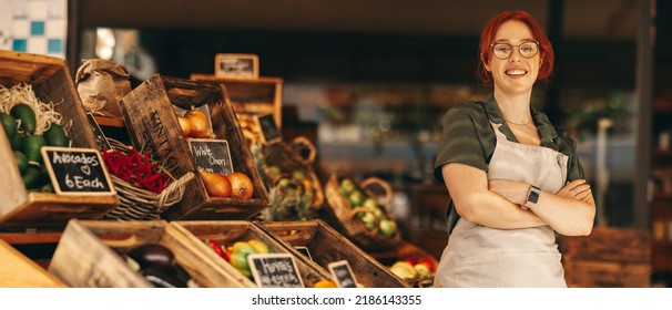Happy supermarket owner smiling at the camera while standing in the fresh produce section of her grocery store. Successful young woman running a small business in the food industry. - Powered by Shutterstock