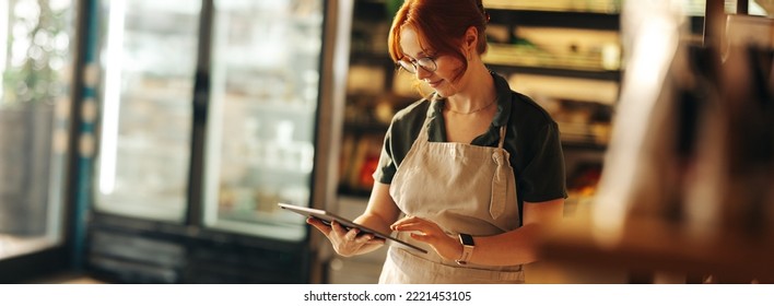 Happy supermarket owner using a digital tablet while standing in her grocery store. Successful entrepreneur running her small business using wireless technology. - Powered by Shutterstock