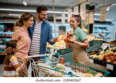 Happy supermarket worker offering fresh apples to a family who is shopping in supermarket.  - Powered by Shutterstock