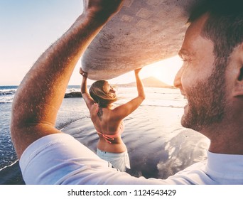Happy surfer couple bringing surf board on the beach - Tourists having fun doing extreme sport in vacation - Relationship and travel lifestyle concept - Main focus on girl's head - Powered by Shutterstock