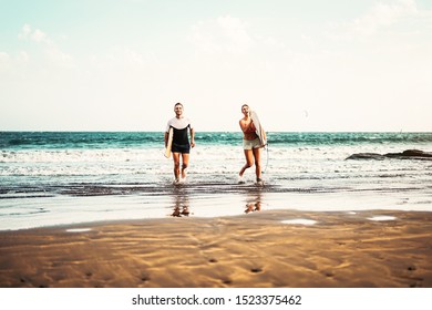 Happy Surfers Couple Running Out Water After Ride On Waves - Young People Having Fun Surfing Together - Extreme Sport And Youth Culture Lifestyle Concept 