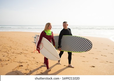 Happy surfers going away from beach and talking. Smiling man and woman holding surfboards and looking at each other. Vacation, surfing and summer concept - Powered by Shutterstock