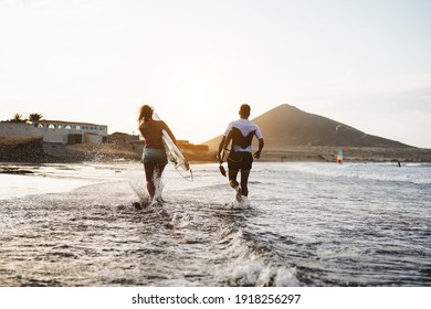 Happy Surfers Running In The Water At Sunset Time - Young Couple Having Fun Surfing In Ocean - Extreme Sport And Youth Culture Lifestyle Concept