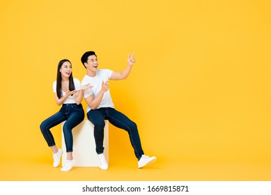 Happy surprised attractive young Asian couple pointing and looking at blank space beside in yellow isolated stuidio background - Shutterstock ID 1669815871