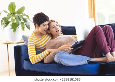 Happy, surprised biracial lesbian couple relaxing on couch using laptop together. Communication, free time, relaxation, relationship, togetherness, domestic life and lifestyle, unaltered. - Powered by Shutterstock