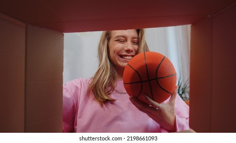 Happy Surprised Winner Girl Unpacking Delivery Parcel At Home. Smiling Satisfied Young Woman Shopper, Online Shop Customer Opening Cardboard Box Receiving Purchase Gift Ball By Fast Postal Shipping