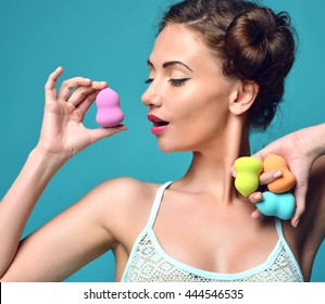 Happy surprised woman hold colorful sponge for applying foundation for make-up on face skin cares on blue mint background
