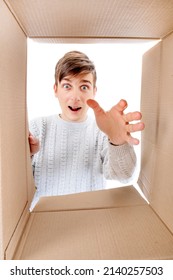 Happy And Surprised Young Man Looking Inside A Box And Reaching A Hand