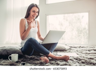 Happy Surprised Young Woman Is Working With A Laptop At Home Sitting On A Carpet