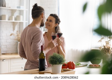 Happy sweet dating couple in love flirting, drinking red wine, cooking dinner in kitchen, enjoying romantic evening, spending leisure time at home together, celebrating anniversary, event - Shutterstock ID 2089628062