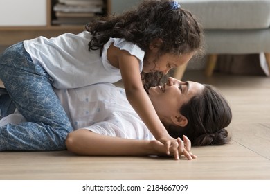 Happy Sweet Loving Little Indian Kid Girl Resting On Laughing Mom Side View. Cheerful Mother Lying On Back On Heating Floor Cuddling, Caressing Sweet Child. Motherhood, Family Leisure Concept