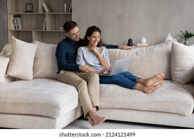 Happy sweet young couple watching movie on laptop, making video call, using online application, shopping online, looking at screen, laughing, sharing computer, relaxing on couch at home - Powered by Shutterstock