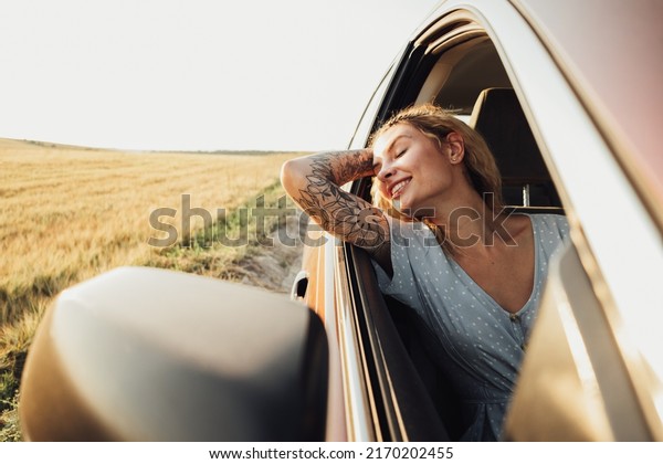Happy Tattooed Girl Enjoying Road Trip,\
Young Woman Relaxing and Looking Out Car\
Window