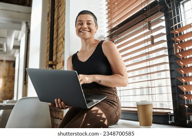 happy tattooed woman using laptop, sitting on windowsill, coffee to go, startup project, coworking - Powered by Shutterstock