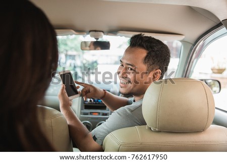 happy taxi driver showing mobile phone to his customer