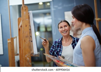 Happy teacher of arts talking to young student about her painting on canvas - Powered by Shutterstock