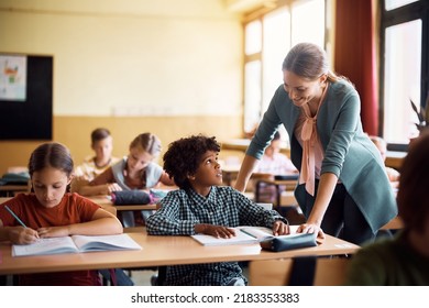 Happy teacher assisting her student during a class at elementary school. - Shutterstock ID 2183353383